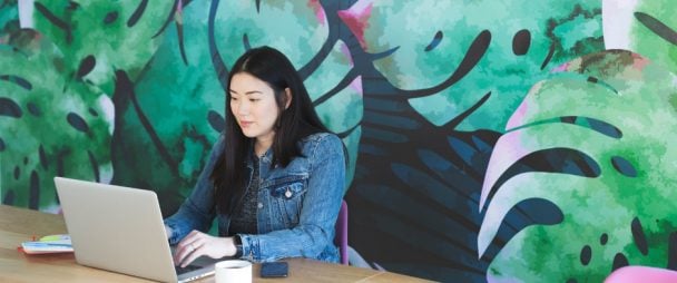 woman working on a laptop in front of a beautiful green-leafed wall