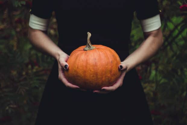 person holding a pumpkin and wearing a black dress and black nail polish