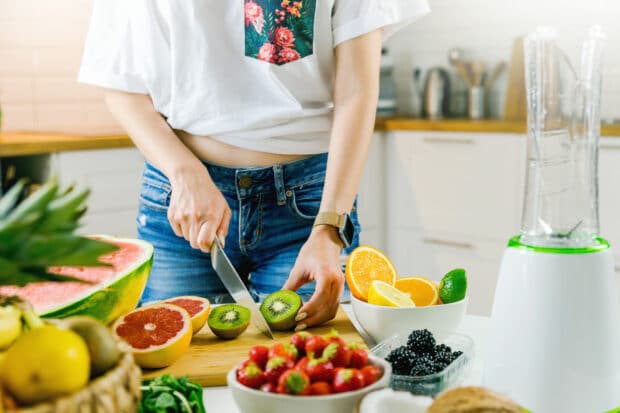 person in kitchen chopping kiwi and other fruit