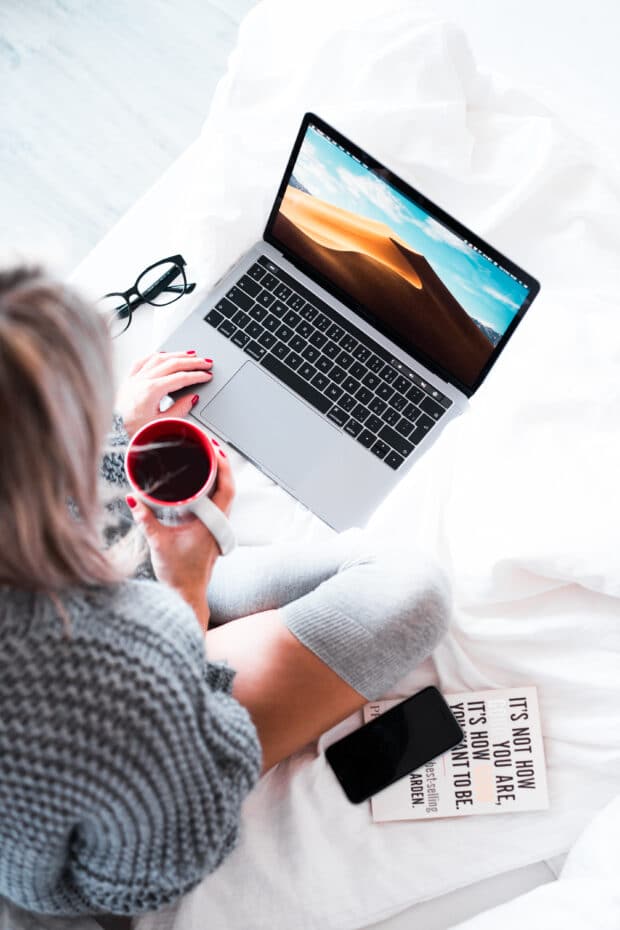 Mujer sosteniendo una taza de café y trabajando en una laptop