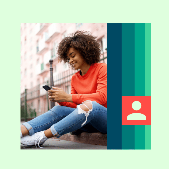 A woman smiles at her mobile device while sitting on a curb.