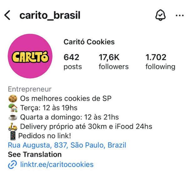 A imagem mostra o perfil da Caritó Cookies, cuja biografia utiliza emojis para cada informação – emoji de cookie e a frase “Os melhores cookies de SP”, emoji de casa e a “Terça: 12 às 19hs”, emoji de xícara e “Quarta a domingo: 12 às 21hs”, emoji de moto e “Delivery próprio até 30km e iFood 24hrs”, emoji de celular e “Pedidos no link!”, além do endereço e do link da marca.