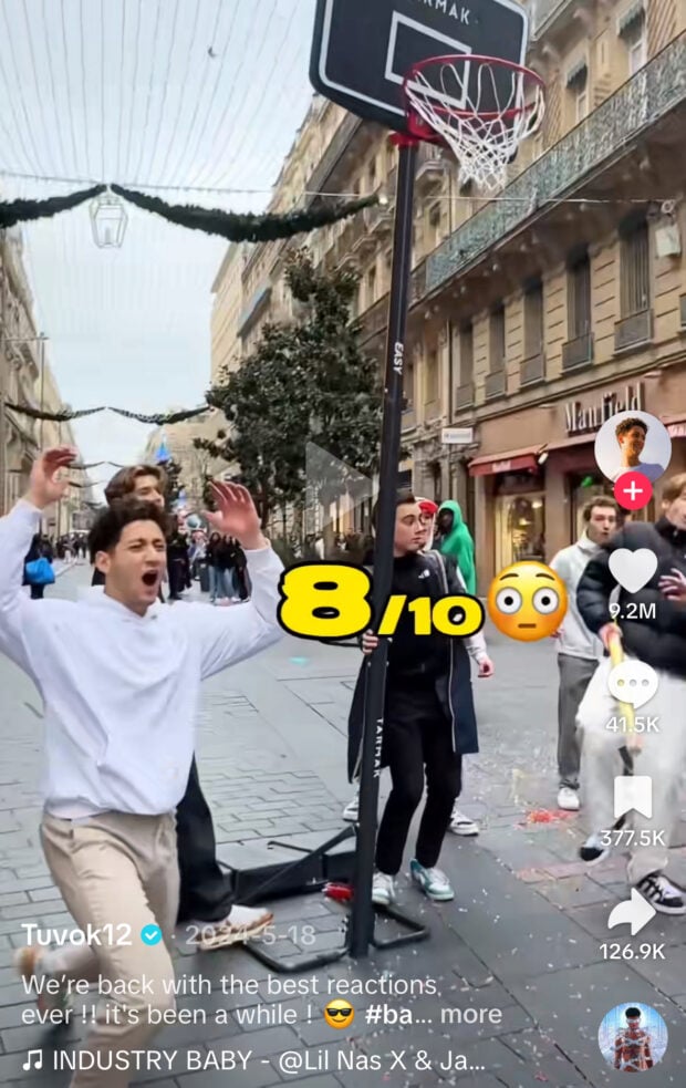 A group of young men react dramatically after a basketball shot in a European shopping street. The screen reads “8/10 😳” as confetti covers the ground.