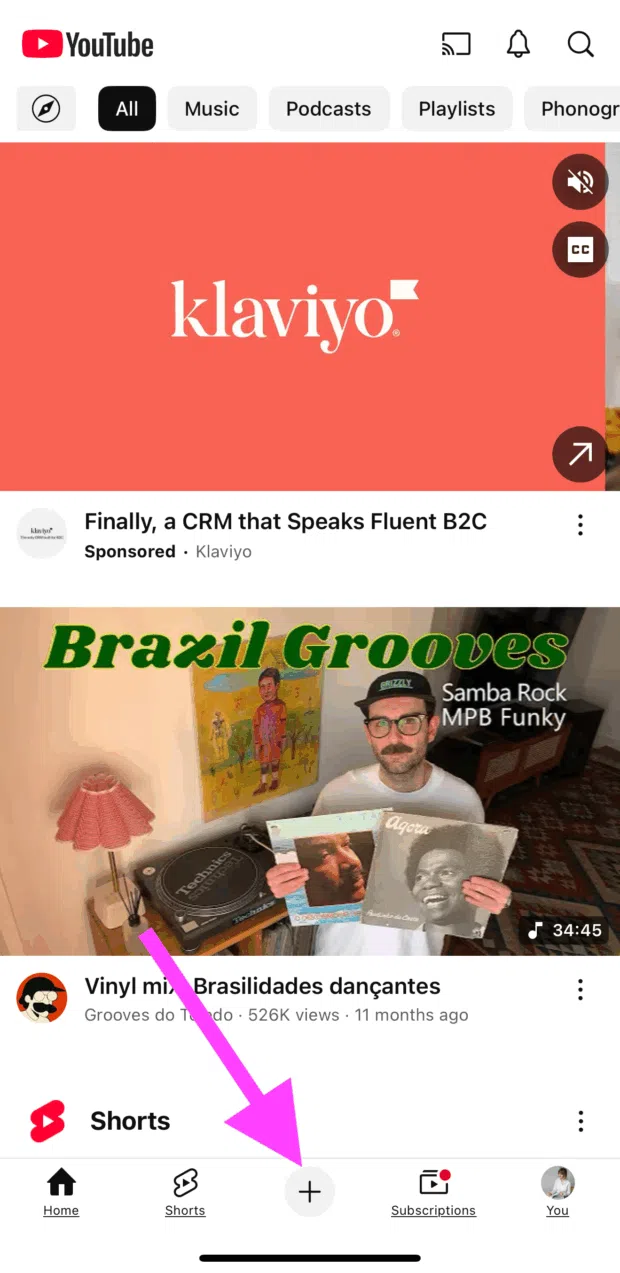Youtube shorts mobile screen showing an ad from klaviyo and a brazil grooces vinyl video with pink arrow pointing to plus button at bottom of screen