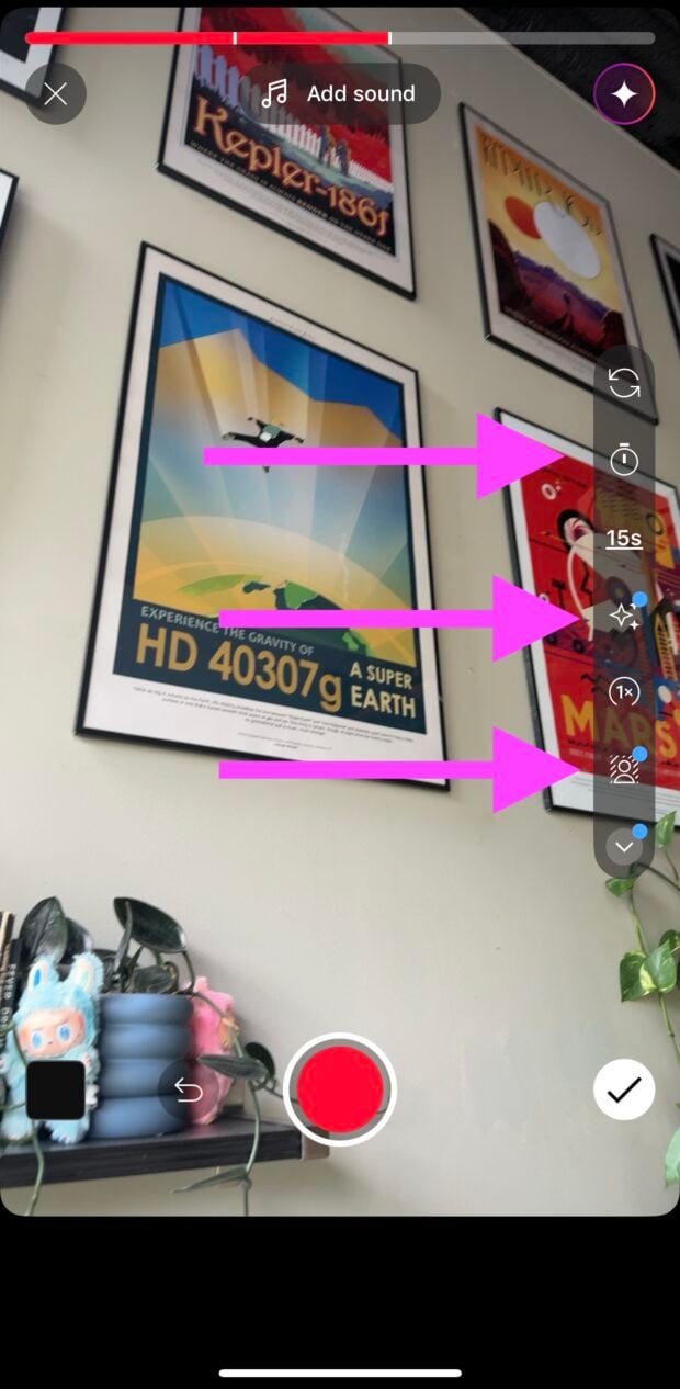 YouTube Shorts recording screen with pink arrows pointing to the progress bar at the top, the 15-second timer icon, the sparkle effects icon, and the speed control icon on the right. Framed space-themed posters are visible on the wall. A shelf with plants, books, and plush toys appears at the bottom