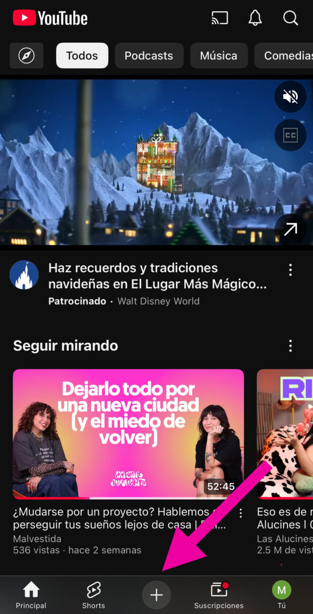 Pantalla móvil de YouTube Shorts con una flecha rosa que apunta al botón más en la parte inferior de la pantalla