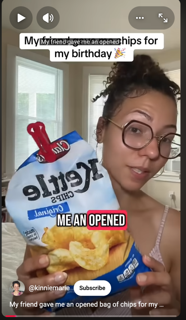 Screenshot of a YouTube Short by @kinniemarie. A woman holds up an open, clipped bag of Kettle Chips Original. On-screen text reads: "My friend gave me an opened bag of chips for my birthday." The word "OPENED" is highlighted in red.